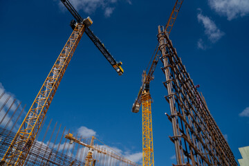 Yellow big industrial construction cranes working on building big city complexes with summer blue skies in the background