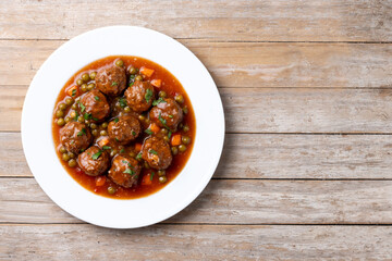 Meatballs, green peas and carrot with tomato sauce on wooden table. Top view. Copy space