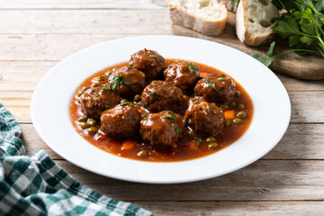 Meatballs, green peas and carrot with tomato sauce on wooden table