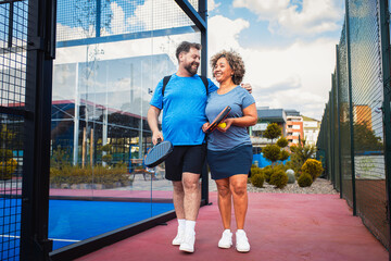 Smiling mix couple comes to the outdoor court to play padel.