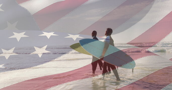 Image of american flag over senior african american couple walking on beach with surfboards