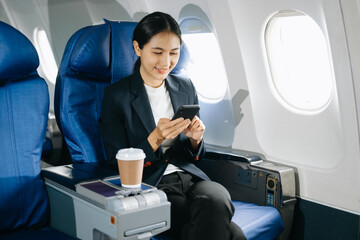 Young Asian executive excels in first class, multitasking with digital tablet, laptop and...