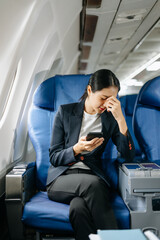 Attractive Asian female passenger of airplane sitting in comfortable seat while working laptop and tablet with mock up area using wireless connection.