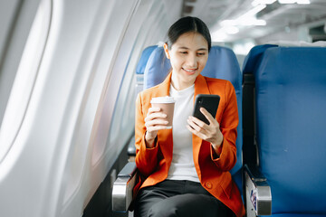 Young Asian executive excels in first class, multitasking with digital tablet, laptop and...