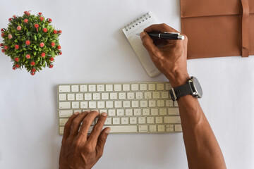 Asian man hand typing on keyboard and writing notepad flat lay or top down view from above