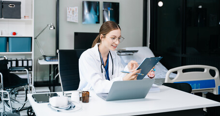 Young female doctor in white medical uniform using laptop and tablet talking video conference call...