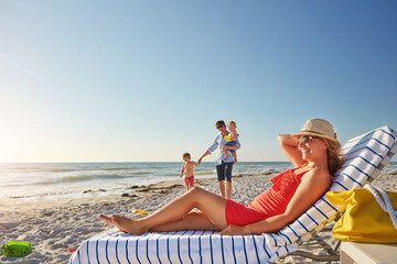 Woman, blue sky and relax on beach chair with family together, adventure and bonding in summer holiday. Happy, mother and sunglasses by ocean, travel and freedom for tropical vacation in Greece