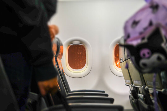 A passenger stands up to exit the plane after landing, holding a water bottle and wearing a backpack, capturing the moment of travel transition inside the aircraft.