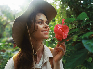 A woman wearing a hat is holding a flower in her hand and looking at it