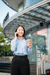 Asian woman with a smile standing holding notepad and tablet at out side office. big city on...