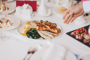 Waiter serving table in the restaurant preparing to receive guests. Waiter carrying plates with meat dish on some festive event. 