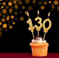 Number 130 birthday candle - Cupcake on black background with out of focus lights