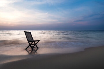 A wooden chair is sitting on the beach, facing the ocean. Pantai Kartini beach
