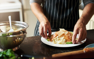 Person, plate and cooking food in home for dinner or eating on kitchen counter with pasta and cheese. Male chef, dish and meal prep for lunch, wellness and brunch with salad for dining in house