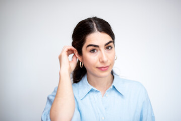 beautiful brunette woman with light blue shirt   adjusting hair with hand on white background 