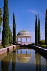 Picturesque white gazebo reflecting in water surrounded by cypress trees in a sunny day