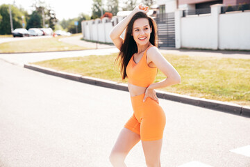 Young beautiful smiling female in trendy summer cycling shorts and tank top clothes. Carefree woman posing in street. Positive model having fun. Cheerful and happy. Sits on asphalt