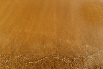 sandy beach with waves rolling in, creating a beautiful natural background. beige sand contrasts with ocean waves. concept for perfumes, smells, heat, freshness, coolness and other associations