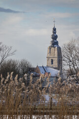 Winter view towards Mespelare and St. Aldegonde Church, near Dendermonde in Belgium. Looking across the River Dender through the side lit grasses on the riverbank with snow on the church. Copy space.