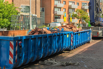 two long blue open industrial steel containers filled with roof tile waste