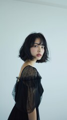 Fototapeta premium Elegant portrait of a young Asian woman with a black bob haircut, wearing a black dress. Minimalistic portrait of a Japanese young woman in a light studio