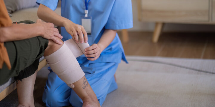 Close up of Asian caregiver bandaging elderly woman's leg at home. Concept of elderly care and wound management