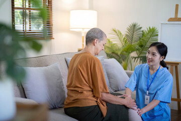 Obraz premium Asian caregiver kneeling beside elderly woman on couch at home. Concept of elderly care and support