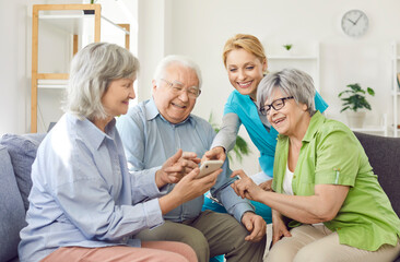 Obraz premium Group of senior patients in a nursing home enjoying leisure time with a caregiver or nurse. Using a mobile phone to go online, showcasing the elderly engaging with modern technology and the internet.
