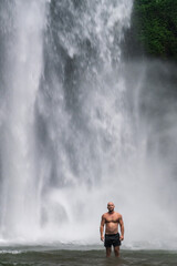 Obraz premium Muscular Man Raising Hand Toward Waterfall in Jungle