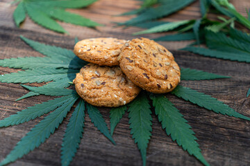 Marijuana leaf and sweets on wooden brown table. Cannabis flowers and cookies close up. Hemp recreation, canna kitchen, pastime, legalization concept.