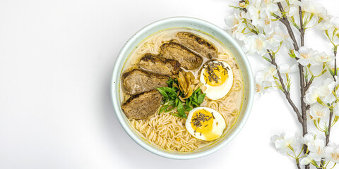Japanese noodles Ramen with broth. Hot dish, duck, egg, greens. White background, cherry flowers