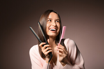 Beautiful young woman with hair straightener and comb on pink background