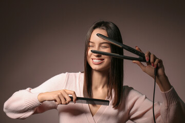 Beautiful young woman with hair straightener and comb on pink background