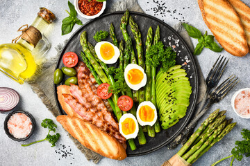 Nutritious Breakfast: green asparagus, avocado, chicken eggs and bacon. In a stone plate.