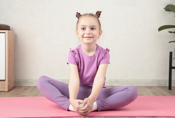Naklejka premium Charming little girl is smiling while doing yoga. Vertical photo