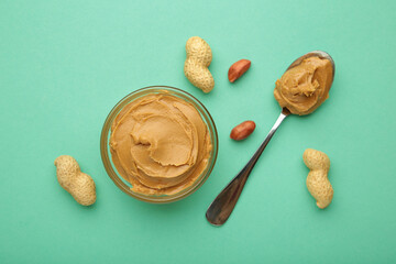 Bowl of peanut butter and peanuts on mint background. Creamy peanut pasta in small bowl.