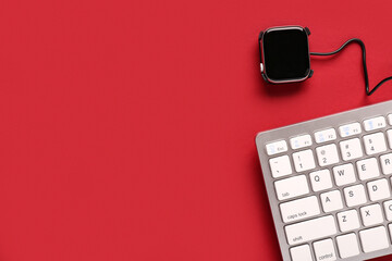 Smart watch with charging cable and computer keyboard on red background. Top view