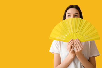 Young woman with hand fan on yellow background