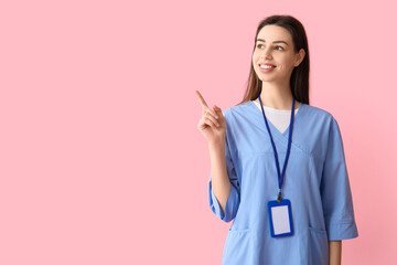 Young female doctor pointing at something on pink background