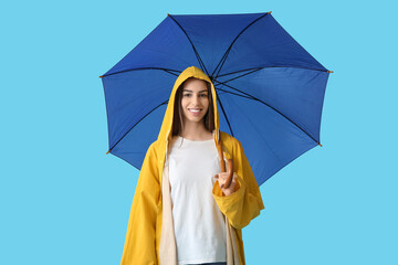 Young happy woman in raincoat with opened umbrella on blue background