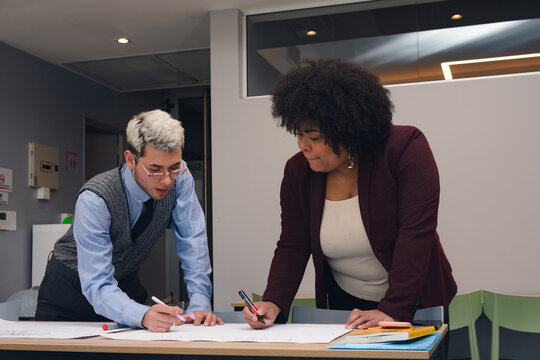 Two young people are working together on a project they are talking and taking notes on a paper
