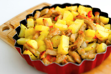 Roasted Potatoes and Pork in a Red Dish on a Wooden Cutting Board