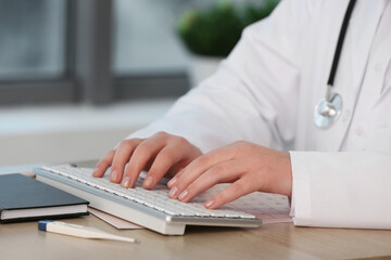Female doctor working with computer keyboard at wooden table, closeup