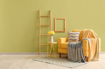 Obraz premium Cozy armchair with plaid, ladder and daffodil flowers in living room