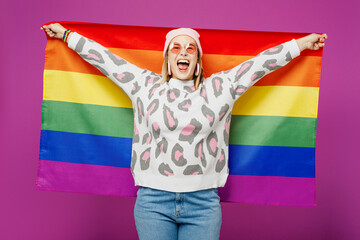 Young excited lesbian woman she wear pink animal clothes hold striped colorful rainbow flag behind...