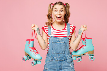 Young shocked surprised excited woman she wear red t-shirt denim overalls casual clothes hold blue rollers look camera isolated on plain pastel pink background. Summer sport lifestyle leisure concept.