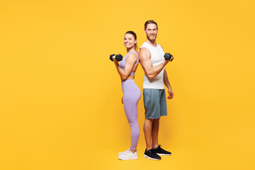 Full body side view young young strong fitness trainer sporty two man woman wear blue clothes spend time in home gym holding in hand dumbbells isolated on plain yellow background Workout sport concept