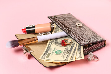 Wallet with beautiful earrings, rings, money, lipstick and makeup brush on pink background