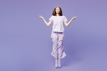 Full body young calm woman wears pyjamas jam sleep eye mask rest relax at home jump high hold spreading hands in yoga om aum gesture isolated on plain purple background. Good mood night nap concept.