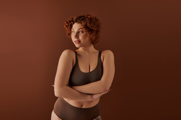 A young curvy redhead woman exudes confidence, posing in a brown bikini.